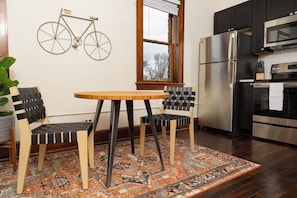 Une cuisine avec une table ronde en bois, deux chaises, un réfrigérateur et un four à micro-ondes.