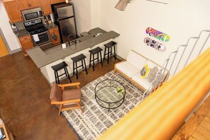 Eine kompakte Küche mit modernen Geräten, ein Essbereich mit Hocker, eine Couch und ein gemustertes Teppich.
