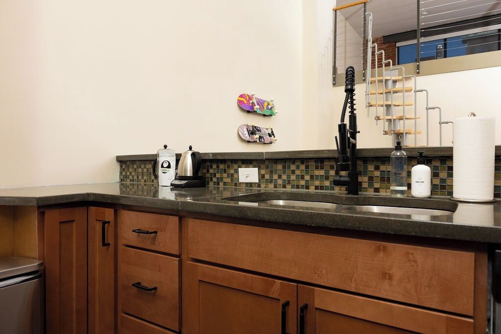 A kitchen with a tiled backsplash, wooden cabinets, a stainless steel sink, and a coffee maker.