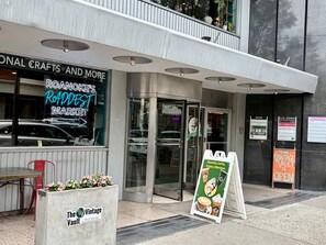 A storefront with a neon sign for Roanoke's Raddest Market, a glass door entrance, and a sign for The Vault. - Stay Roanoke | Historic brick charm 1BR downtown (Roanoke)