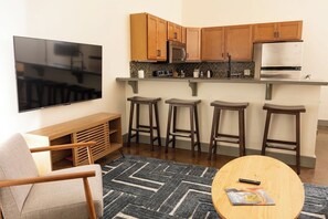 A compact living space with a kitchenette, a flat-screen TV, a sofa, and a coffee table. - Stay Roanoke | Historic brick charm 1BR downtown (Roanoke)
