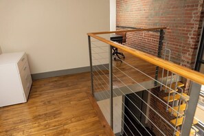 A staircase with a wooden handrail, a white cabinet, and a brick wall. - Stay Roanoke | Historic brick charm 1BR downtown (Roanoke)