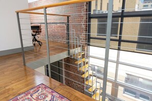 A modern interior with a wooden floor, a metal staircase, and a large window offering a view of the outside. - Stay Roanoke | Historic brick charm 1BR downtown (Roanoke)