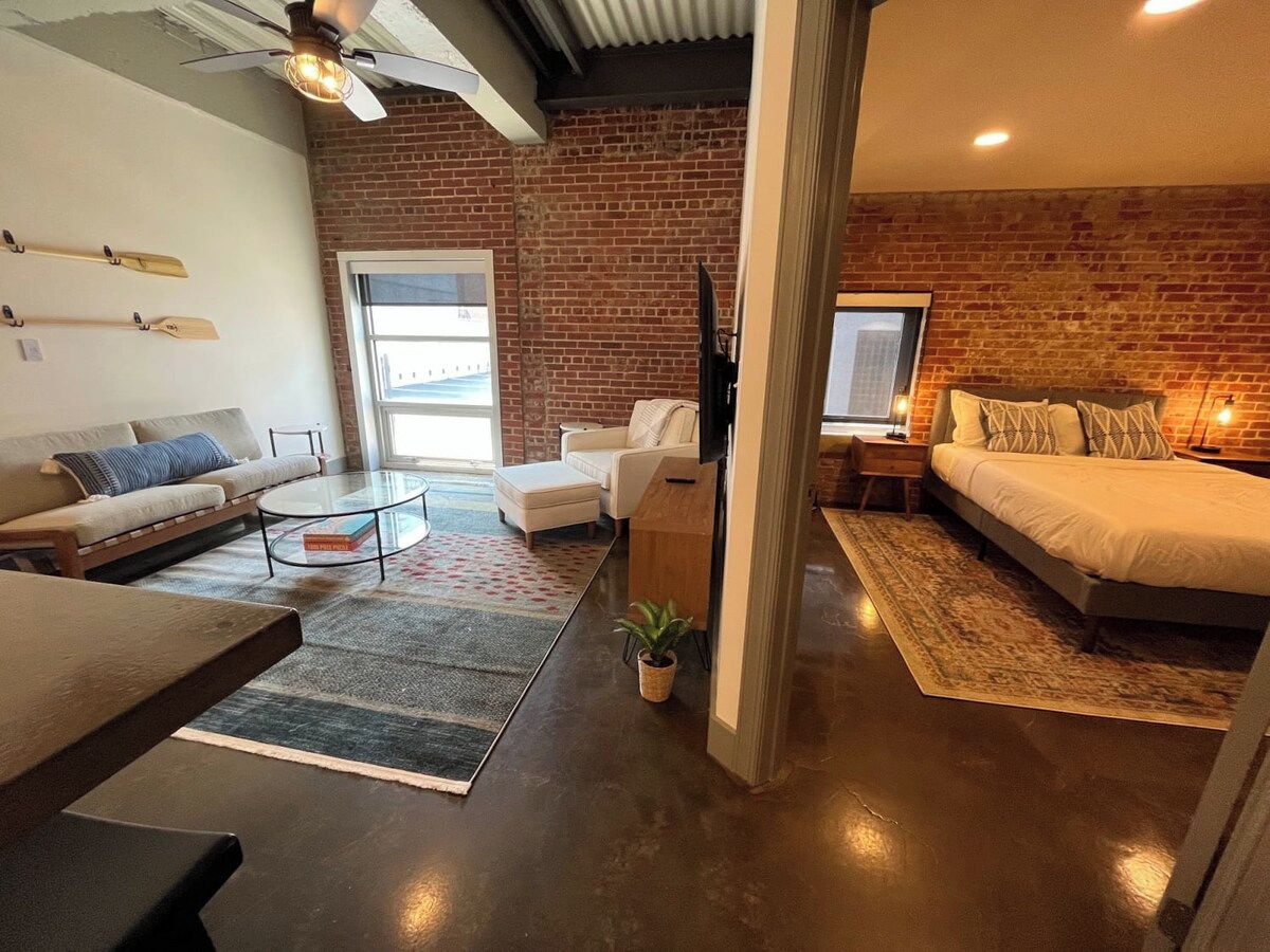Un salon moderne avec un mur en briques, un canapé, une table basse et un téléviseur.