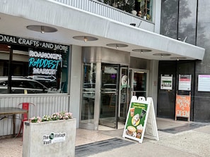 A storefront with a neon sign for Roanoke's Raddest Market, a glass door entrance, and a sign for The Vault. - Stay Roanoke | Downtown 2BR w/exposed brick charm (Roanoke)