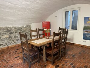 Uma área de refeições com mesa e cadeiras de madeira, geladeira vermelha, parede de pedra e janela com pôster.