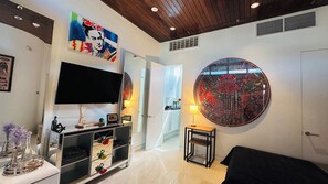 A modern living room with a flat-screen TV, a round mirror, and a dining area with a table and chairs. - Frida Kahlo private 1-bedroom loft  in vibrant Houston (Houston)