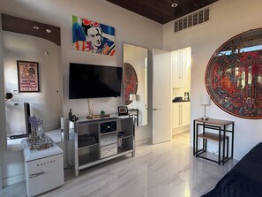 A modern living room with a flat-screen TV, a Galanz refrigerator, a coffee machine, and a large mirror reflecting a vibrant artwork. - Frida Kahlo private 1-bedroom loft  in vibrant Houston (Houston)