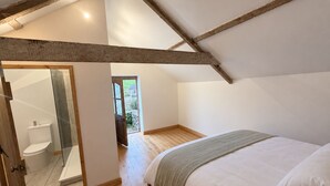 Une chambre avec un plafond en bois, un lit recouvert de linge de lit blanc et une vue sur un jardin par une porte ouverte.