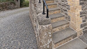 Un bâtiment en pierre doté d’une porte en bois et d’un escalier en pierre menant à une rambarde en métal.