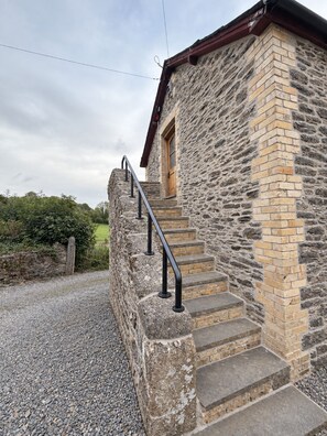 Un bâtiment en pierre doté d’une porte en bois et d’un escalier en pierre menant à une rambarde en métal.