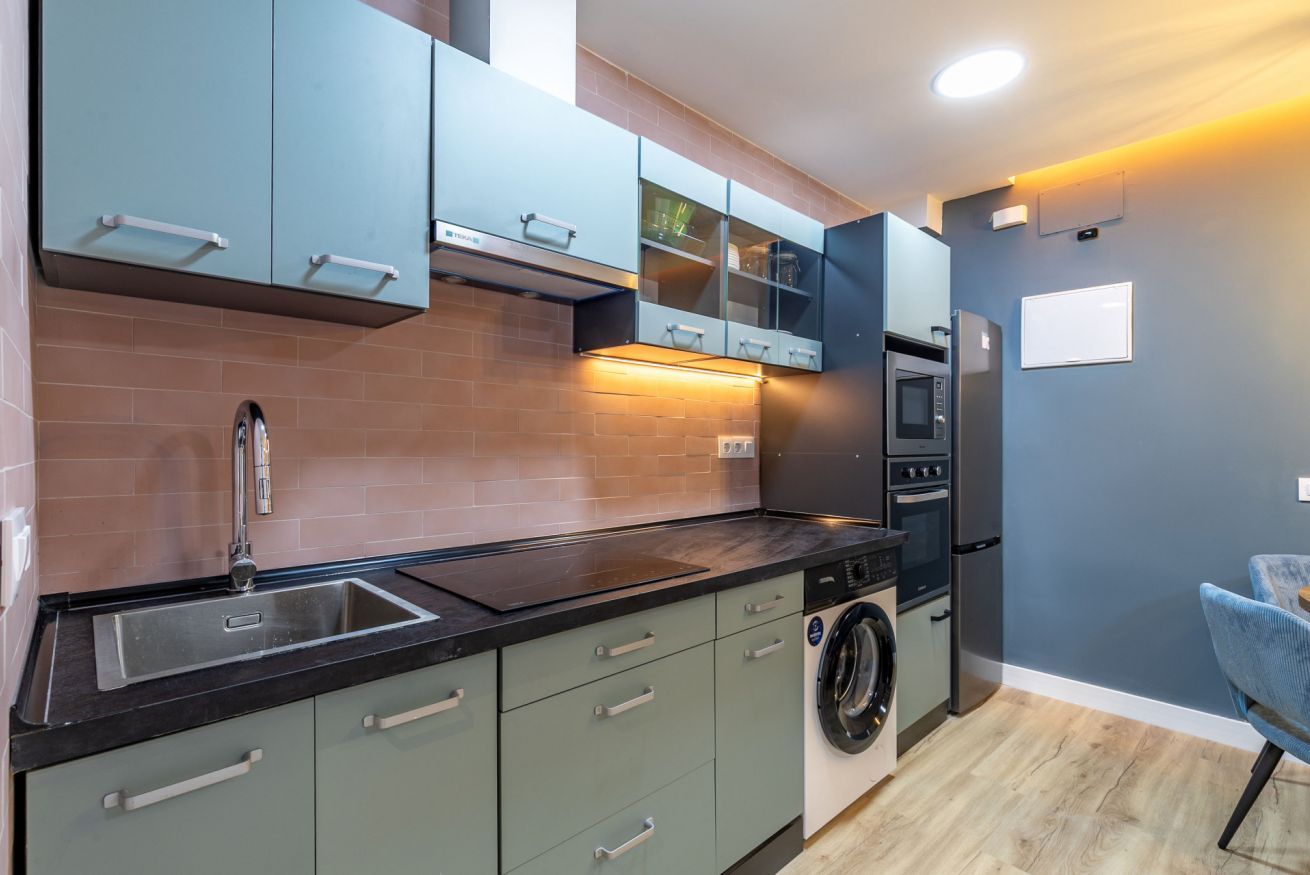 Una cocina moderna con gabinetes grises, una encimera negra, lavadora integrada y horno empotrado.