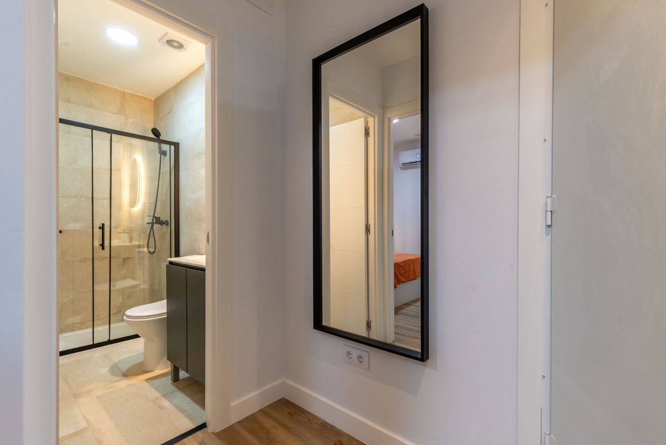 Un baño con cabina de ducha de vidrio, un inodoro y un espejo grande en la pared.