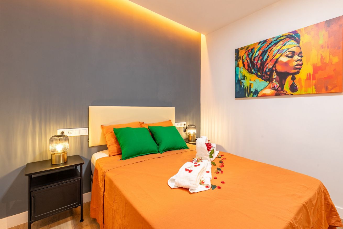 Una habitación de hotel con una cama, almohadas verdes, una mesita de noche con una lámpara y un cuadro en la pared.