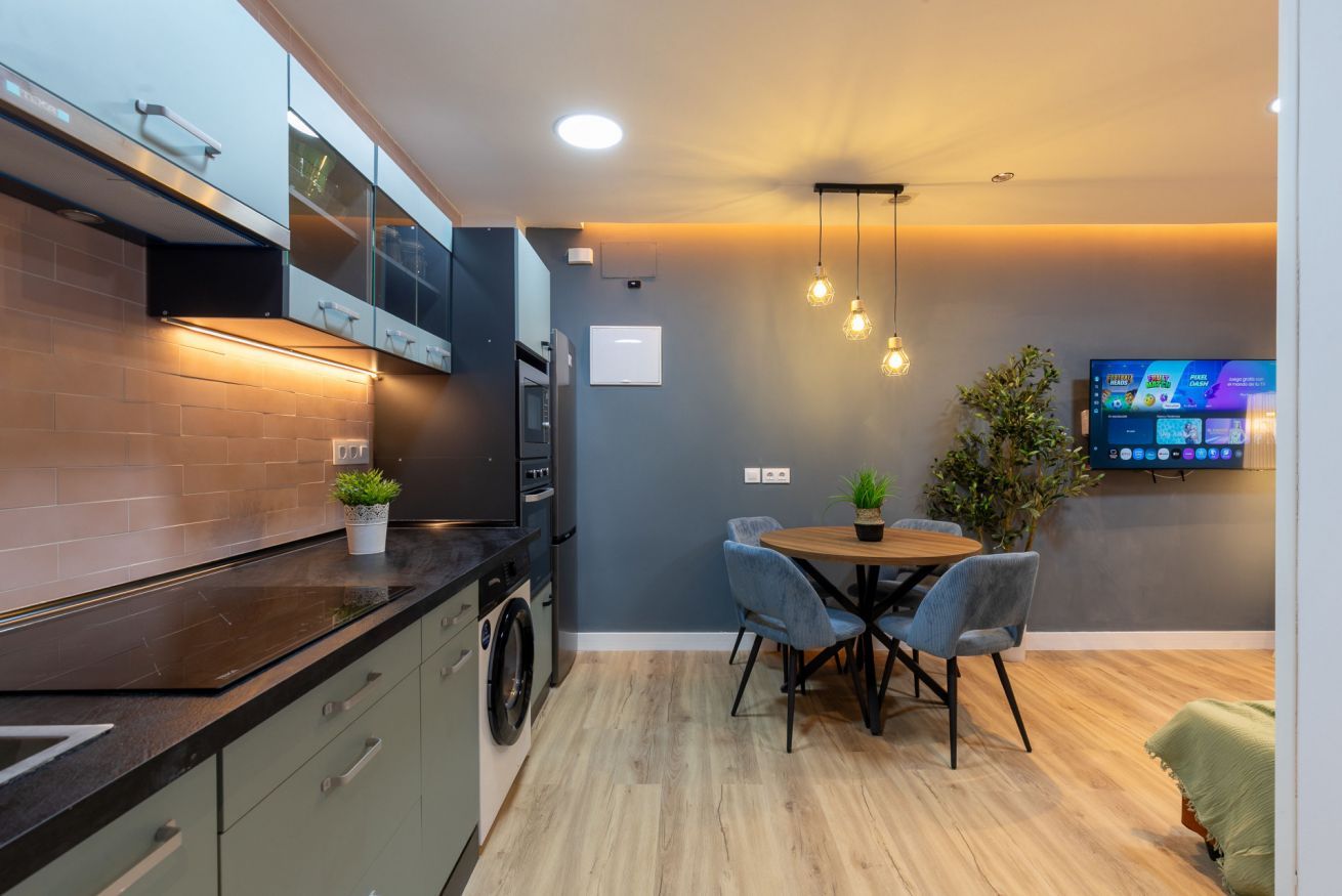 Una cocina moderna con horno integrado, una mesa de comedor con sillas y un televisor de pantalla plana montado en la pared.