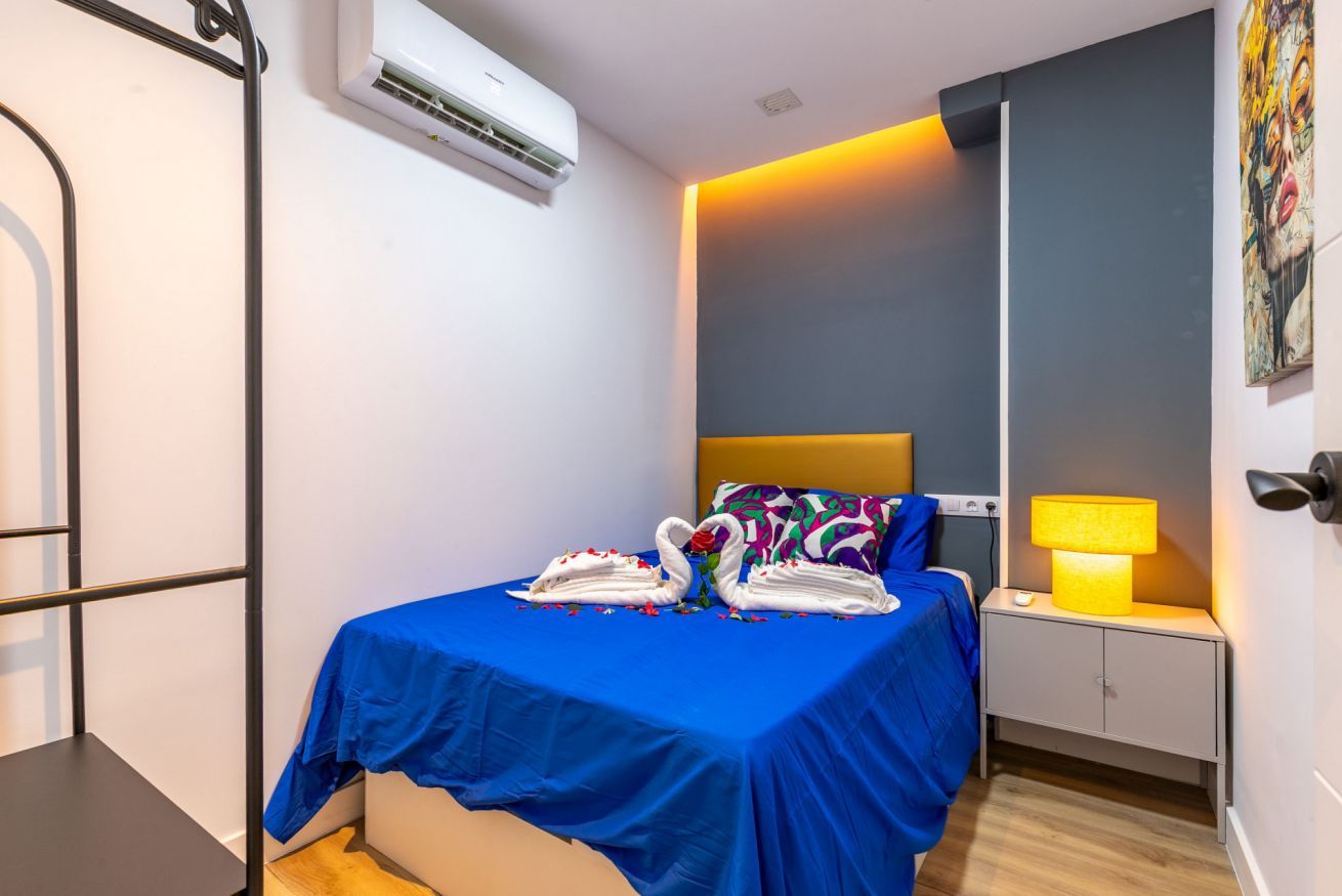 Habitación de hotel con una cama, una mesita de noche con lámpara, un equipo de aire acondicionado y una pared con un cuadro.