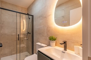 A modern bathroom with a glass shower enclosure, a white sink with a round mirror, and a potted plant. - Appartement 2 chambres moderne et calme - Marqués Vadillo (Madrid)