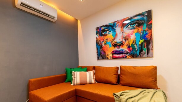 Ein modernes Wohnzimmer mit einem Ecksofa, einem farbenfrohen abstrakten Gemälde und einer Wand-Klimaanlage.