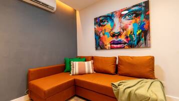 Una sala de estar moderna con un sofá seccional, un cuadro abstracto colorido y un aire acondicionado instalado en la pared.