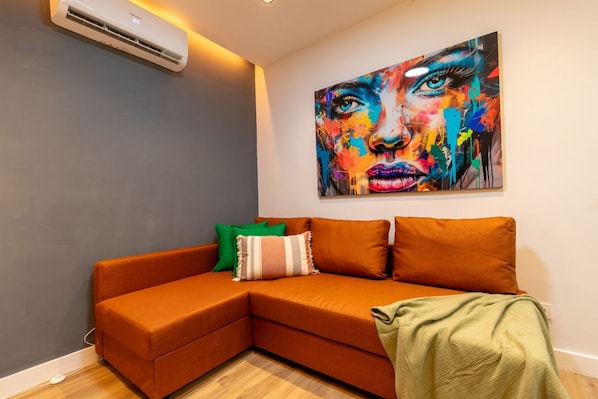 A modern living room with a sectional sofa, a colorful abstract painting, and a wall-mounted air conditioner. - Appartement 2 chambres moderne et calme - Marqués Vadillo (Madrid)