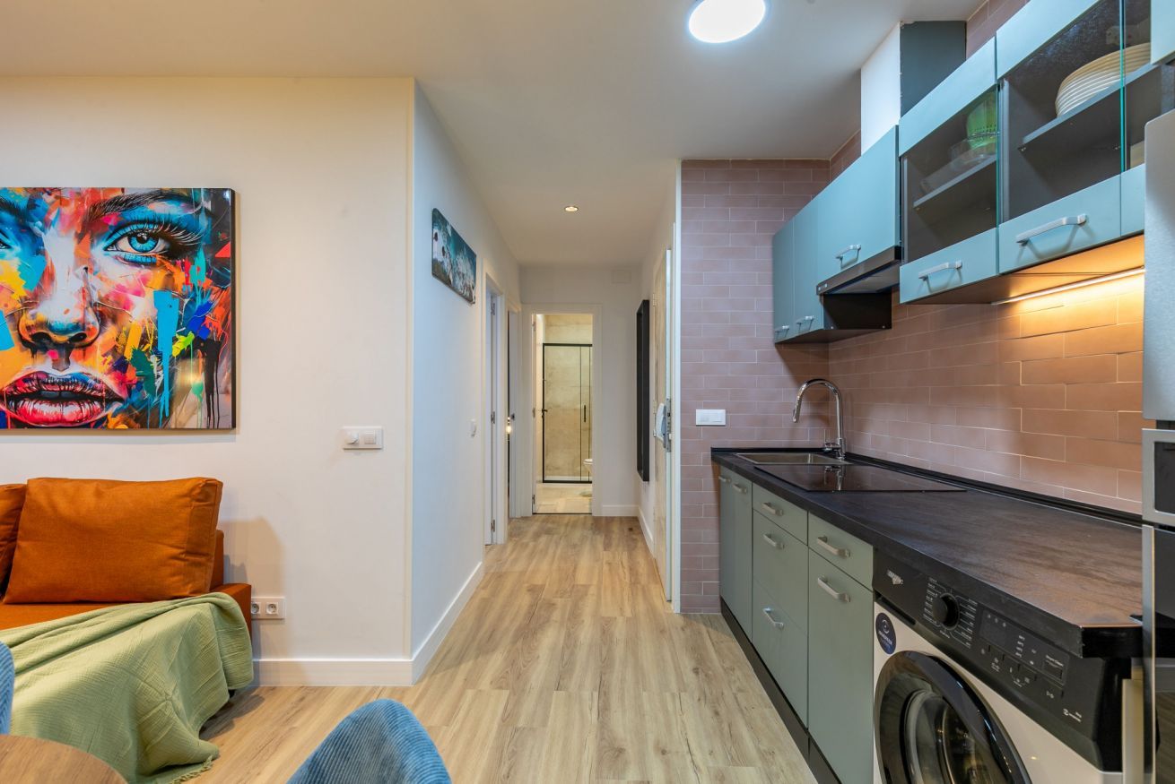 Una cocina moderna con lavadora, una zona de comedor con sofá y un pasillo que lleva a un baño.