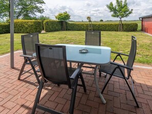 An outdoor patio with a table and chairs, surrounded by a hedge and a view of the countryside. - Holiday Apartment With 2 Bedrooms (Esens)
