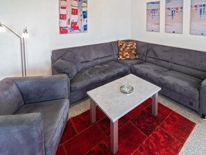 A modern living room with a grey sectional sofa, a small square coffee table, and a red patterned rug. - Holiday Apartment With 2 Bedrooms (Esens)