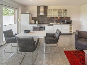 A modern kitchen with white cabinets, a stainless steel range, and a microwave. There is a dining area with a white table and four chairs. - Holiday Apartment With 2 Bedrooms (Esens)