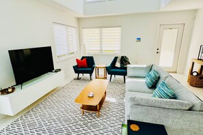 Ein modernes Wohnzimmer mit einem Flachbildfernseher, zwei Sesseln, einer Couch und einem Couchtisch.