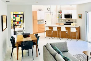 A modern kitchen with a central island, bar stools, and a dining area with a table and chairs. - 708 N Shore in Anna Maria, FL (Anna Maria)