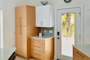 Eine Küche mit Holzschränken, einer weißen Arbeitsplatte, einer gefliesten Spritzschutzwand und einer Tür mit Blick ins Freie.