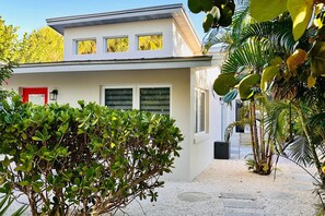 Ein modernes Haus mit weißer Fassade, einer roten Tür und einem kleinen Garten mit verschiedenen Pflanzen.