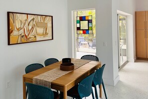 A dining area with a wooden table, teal chairs, a woven placemat, and a framed abstract painting. - 708 N Shore in Anna Maria, FL (Anna Maria)