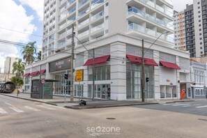 Ein modernes Gebäude mit einem Ladenlokal im Erdgeschoss, mit einem Restaurant namens „Manhattan Love“ und roten Markisen, sowie einem sichtbaren Schild, das eine Geschwindigkeitsbegrenzung von 40 km/h anzeigt.