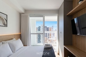 Ein Hotelzimmer mit Bett, Fernseher, Fenster mit Blick auf Gebäude und einem Balkon.
