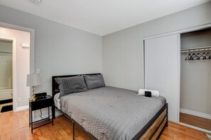 Ein Schlafzimmer mit Bett, Nachttisch, Lampe und einem Kleiderschrank mit Kleidung.
