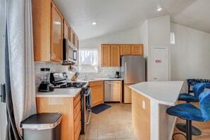 Eine moderne Küche mit Holzausstattung, einem Edelstahlkühlschrank, einem Gasherd und einer Kaffeemaschine.