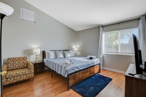 A bedroom with a bed, bedside lamps, a chair, a TV, and a window with blinds. - Experience luxury and convenience in this stylish 3-bedroom, 2-bath home. (North Las Vegas)