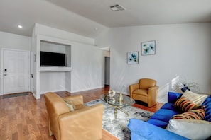 Een woonkamer met een bank, fauteuils, een salontafel en een flatscreen televisie aan de muur.