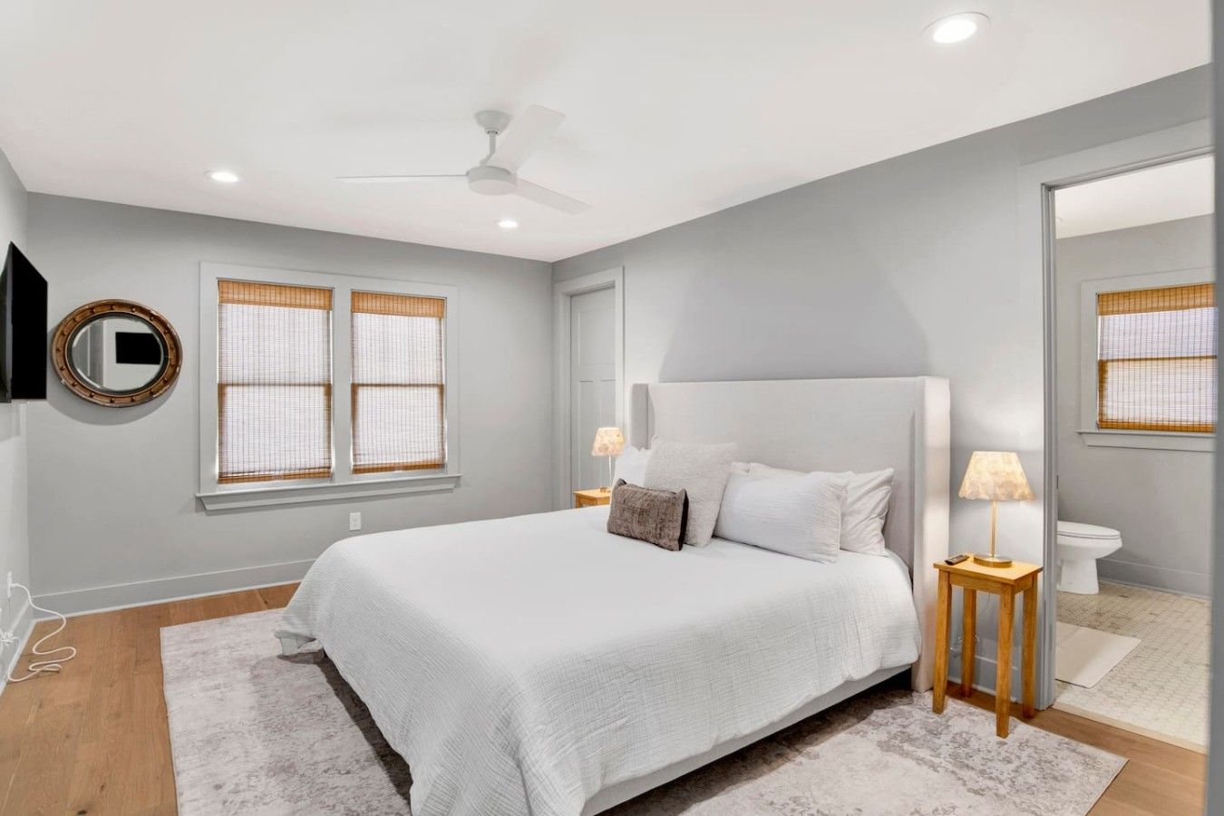 Quarto com cama, luminárias de cabeceira, ventilador de teto e um espelho grande.