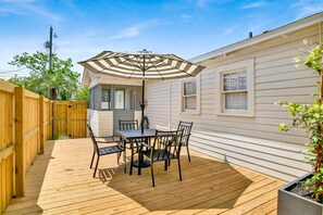 Um deck de madeira com mesa e cadeiras, um guarda-sol listrado e uma casa com janelas.