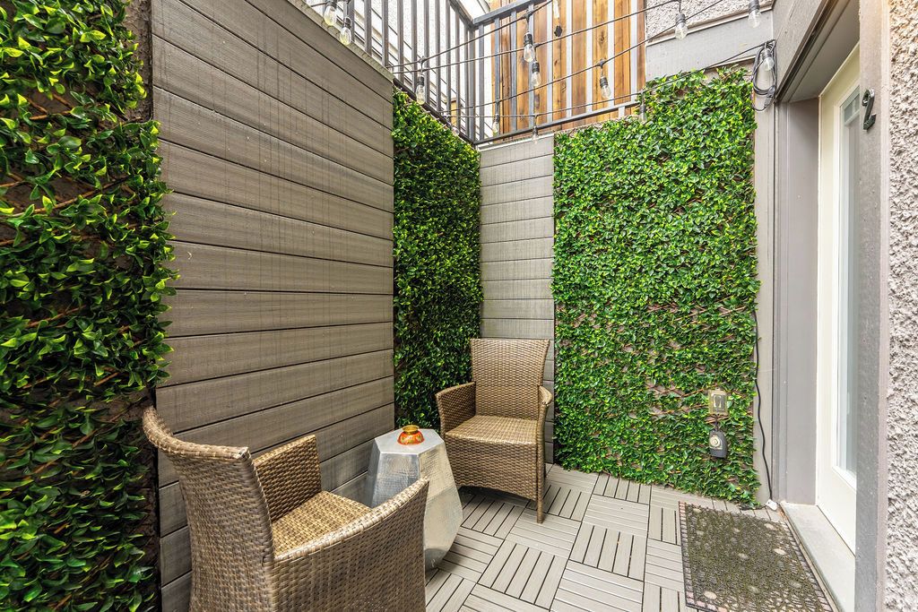 Een klein terras met rieten stoelen en een tafel, omgeven door een houten muur en een verticale tuin.