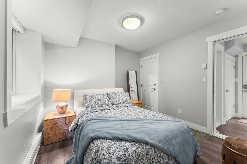 A bedroom with a bed, bedside table, lamp, and a door leading to another room.