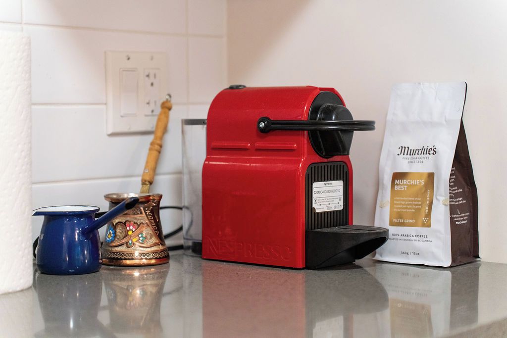 A red Nespresso coffee machine, a blue coffee pot, a traditional copper coffee pot, and a bag of Murchie's coffee on a kitchen counter.