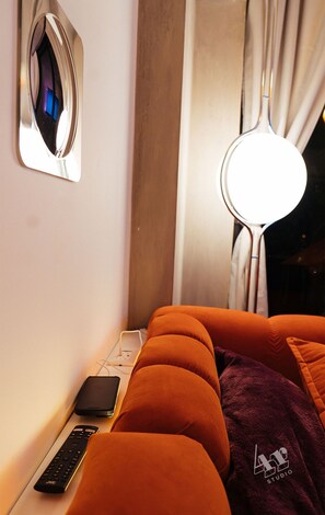 A bed with orange bedding, a bedside table with a remote control, a lamp, and a wall-mounted mirror.