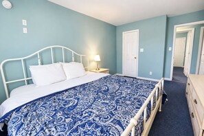 A bedroom with a bed, a bedside table with a lamp, a door, and a dresser. - Parrot Bay Townhouse 30 | Pet Friendly (Ocean City)