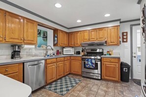 A kitchen with wooden cabinets, stainless steel appliances, and a plaid rug. - Davenport Creek | Dock, Kayaks & Sleeps 12 (White Stone)