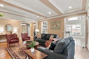 A well-lit living room with a fireplace, a sofa, a coffee table, and a dining area with a lamp. - Hot Tub · Estate on the RTJ Fairway · Sleeps 16+ (Bessemer)