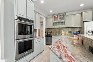 Een moderne keuken met roestvrijstalen apparatuur, marmeren aanrechtbladen en kastjes in een lichte kleur.