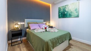 A neatly made bed with a green bedspread, two pillows, and a decorative swan made of towels. There is a nightstand with a lamp and a wall-mounted air conditioner. - Spacious and modern 2-bedroom apartment – ​​Comillas (Madrid)